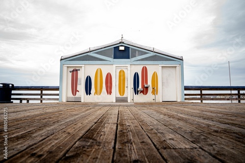 Colorful surfboard-themed building on a wooden pier with an overcast sky in the background