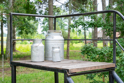 Milk churns sitting on a wooden platform at the side of a country road. Traditional milk churn stand maintained for decorative purposes along a country road.