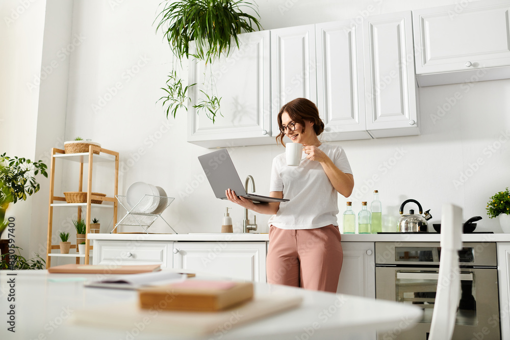 Middle-aged woman standing in kitchen, multitasking with laptop in hand. Middle-aged woman standing in kitchen, multitasking with laptop in hand.