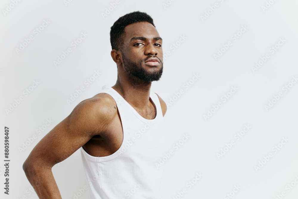 Confident young man in casual white tank top posing against a plain white backdrop with a thoughtful expression Confident young man in casual white tank top posing against a plain white backdrop with a thoughtful expression