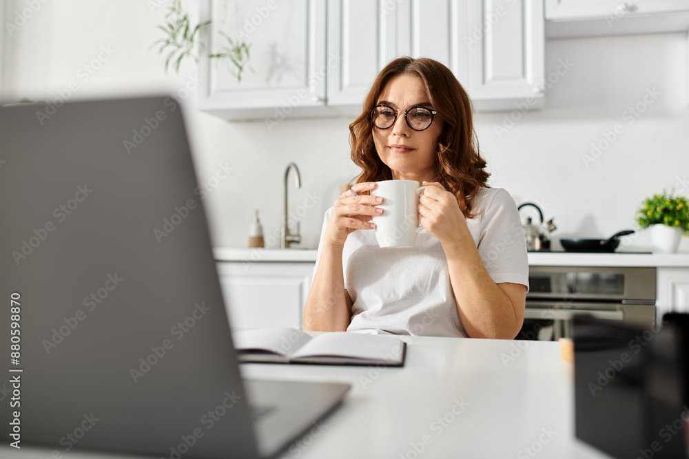 A middle aged woman sits at a table with a laptop and a cup of coffee. A middle aged woman sits at a table with a laptop and a cup of coffee.
