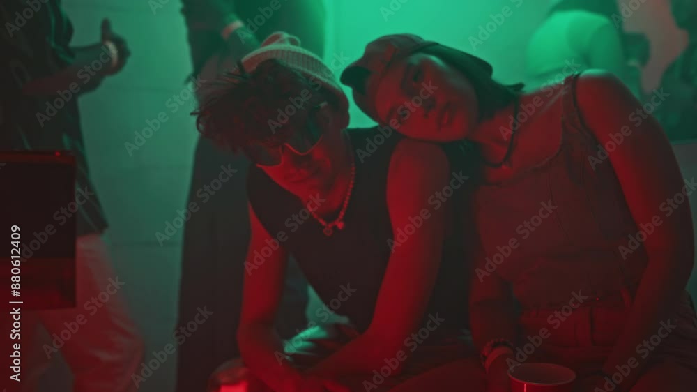 Medium lowkey portrait of trendy Caucasian couple in retro outfits sitting in neon lit nightclub room and looking at camera, gen Z girl putting head on guys shoulder Medium lowkey portrait of trendy Caucasian couple in retro outfits sitting in neon lit nightclub room and looking at camera, gen Z girl putting head on guys shoulder