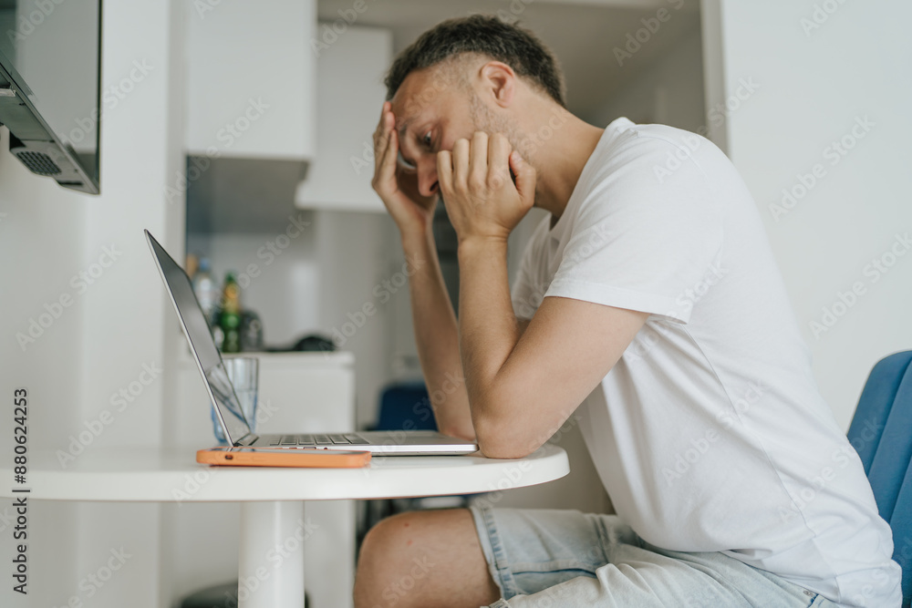 Obraz premium Young man experiencing burnout and stress while working on laptop at home, midlife crisis, mental health issues.
