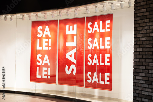 Red sale signs with white lettering are displayed store window. signs are hanging ceiling and visible through glass. concept: sale discounted price off-season discounts black friday