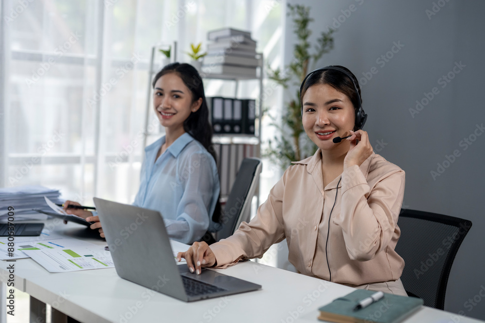 Two women are sitting at a desk with a laptop and a headset Two women are sitting at a desk with a laptop and a headset