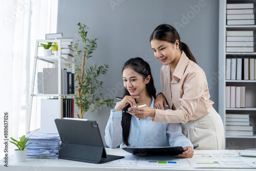 Two women are sitting at a desk with a laptop and a tablet