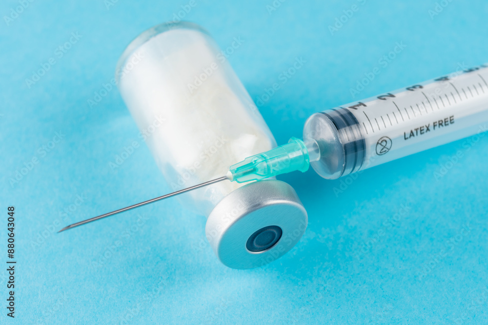 Vaccine vial glass with a syringe on blue background. Vaccine vial glass with a syringe on blue background.