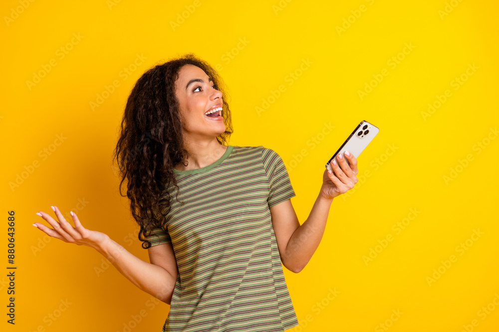 Photo of smart girl with wavy hairstyle dressed striped t-shirt hold smartphone look empty space isolated on yellow color background