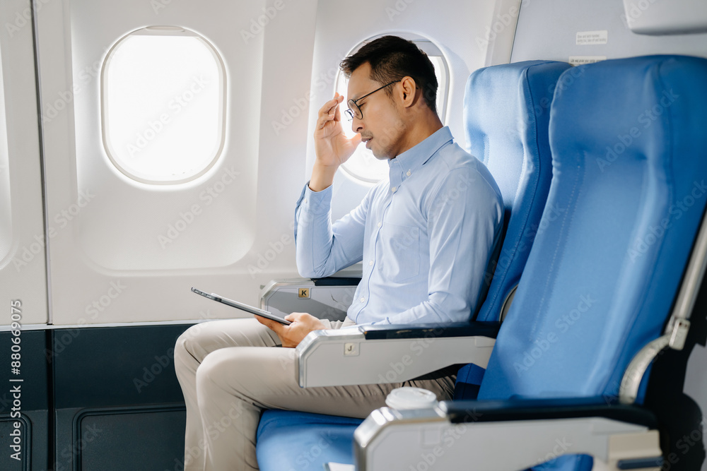 Photo of a frustrated man sitting on an airplane with her head in her hands. Asian Businessman sitting in airplane working Photo of a frustrated man sitting on an airplane with her head in her hands. Asian Businessman sitting in airplane working