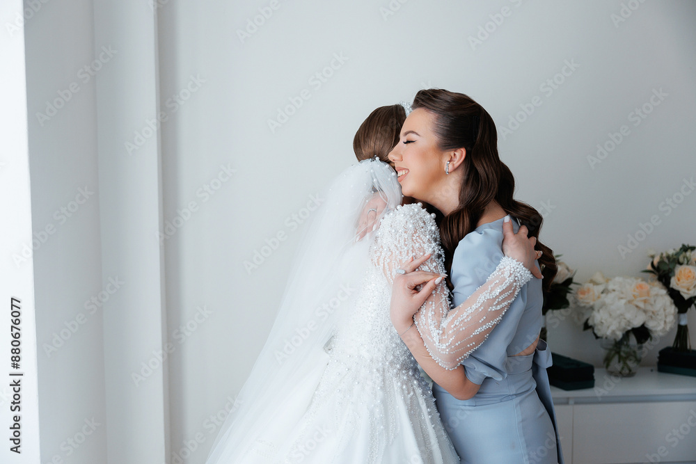 A bride and her bridesmaid are hugging each other. The bride is wearing a white dress and the bridesmaid is wearing a blue dress. Scene is happy and joyful A bride and her bridesmaid are hugging each other. The bride is wearing a white dress and the bridesmaid is wearing a blue dress. Scene is happy and joyful