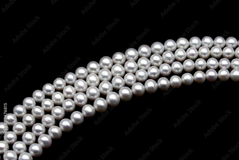 Chinese round freshwater white pearls on strands ready to become a necklace, some of the favorite materials for jewelry on black background. An organic gem that brides love for weddings. Chinese round freshwater white pearls on strands ready to become a necklace, some of the favorite materials for jewelry on black background. An organic gem that brides love for weddings.