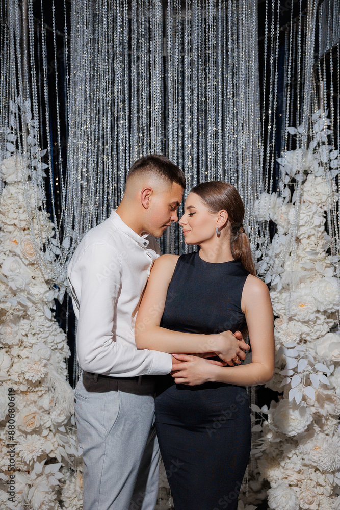 A man and woman are embracing in front of a white backdrop. The man is wearing a white shirt and the woman is wearing a black dress. Scene is romantic and intimate A man and woman are embracing in front of a white backdrop. The man is wearing a white shirt and the woman is wearing a black dress. Scene is romantic and intimate