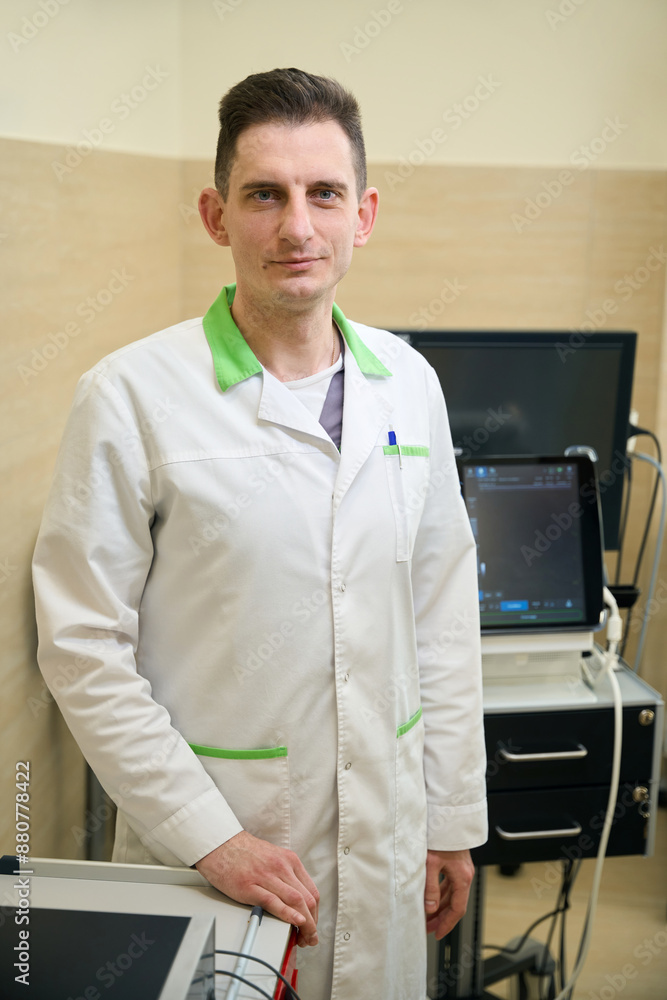 Fototapeta premium Diagnostician posing for camera with ultrasonic medical equipment in background