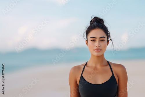 Young Asian woman in athletic wear on a beach, with soft-focus background highlighting the serene and refreshing atmosphere.