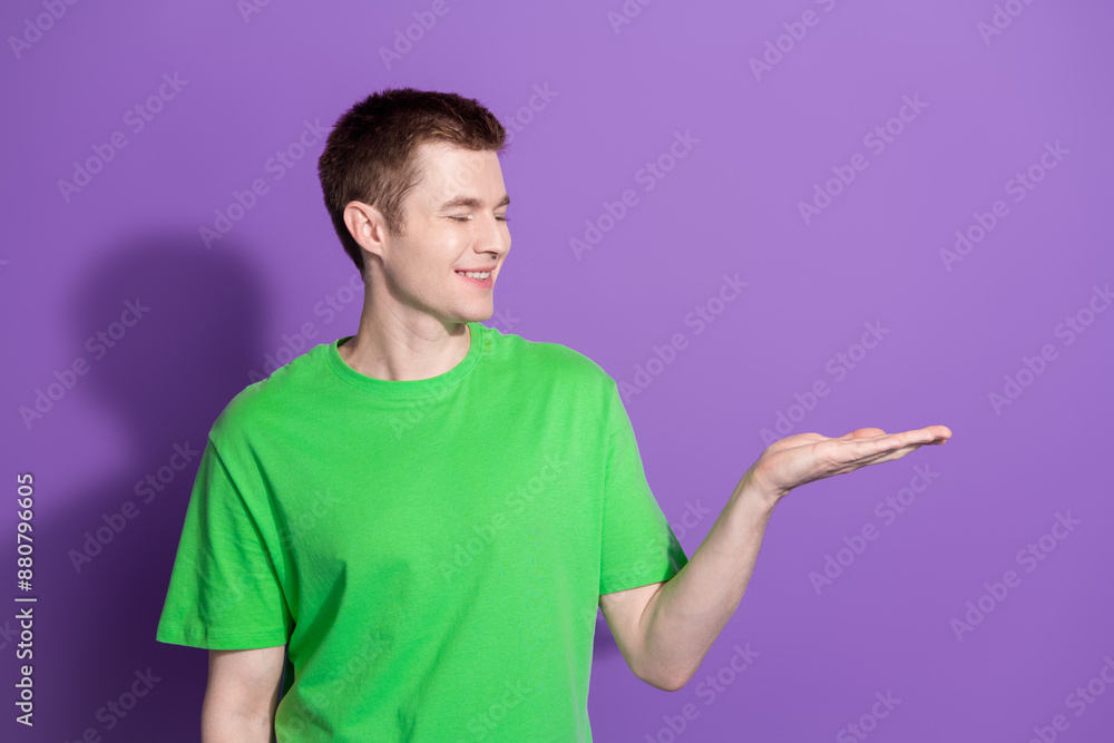 Photo of nice young man arm hold empty space wear t-shirt isolated on violet color background Photo of nice young man arm hold empty space wear t-shirt isolated on violet color background