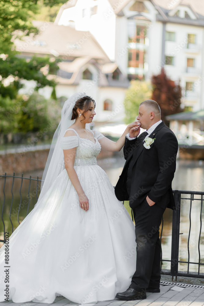 A bride and groom are standing on a bridge, the bride wearing a white dress and the groom wearing a black suit A bride and groom are standing on a bridge, the bride wearing a white dress and the groom wearing a black suit