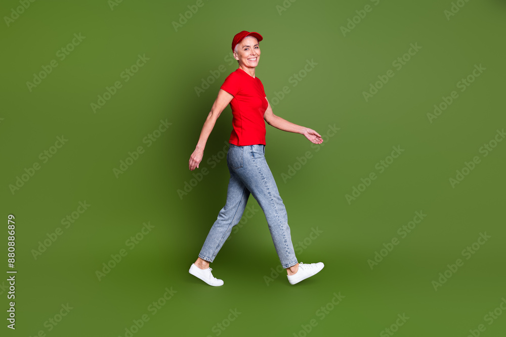 Full length photo of lovely pensioner lady walk delivery service employee dressed red uniform workwear isolated on khaki color background Full length photo of lovely pensioner lady walk delivery service employee dressed red uniform workwear isolated on khaki color background