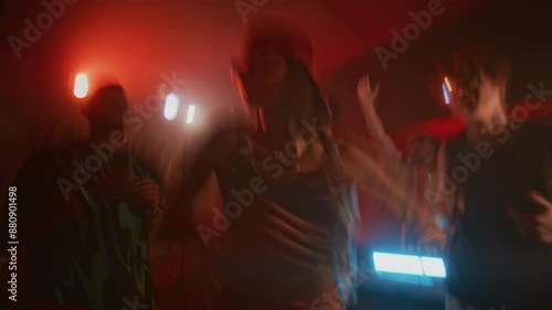 Blurred handheld shot of fashionable lady in y2k outfit actively dancing during retro rave party in nightclub with red neon light and repeated flashes