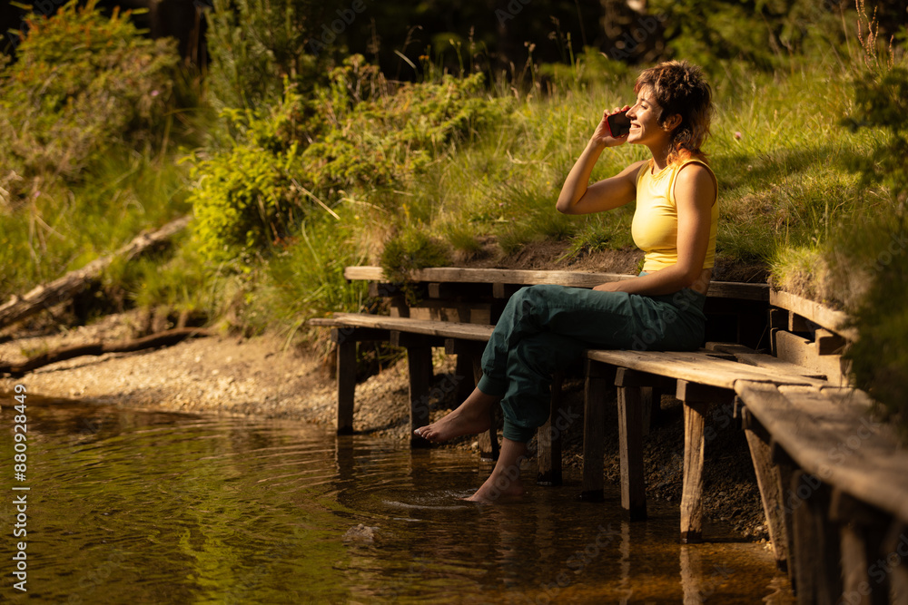 A woman is sitting on a bench by a body of water, talking on her cell phone A woman is sitting on a bench by a body of water, talking on her cell phone
