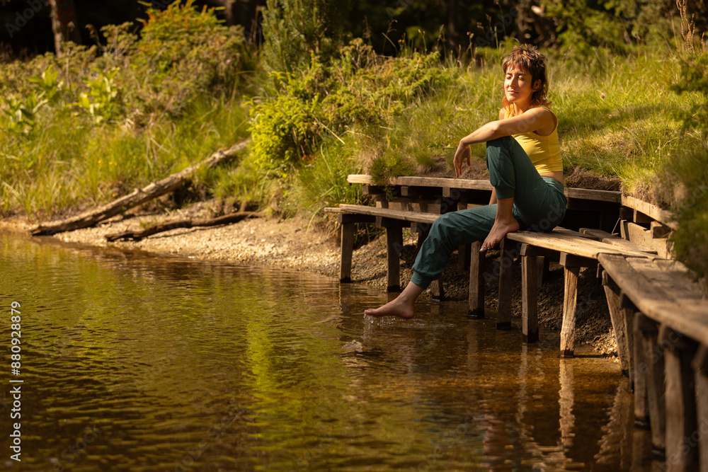 A woman sits on a bench by a lake, looking out at the water A woman sits on a bench by a lake, looking out at the water