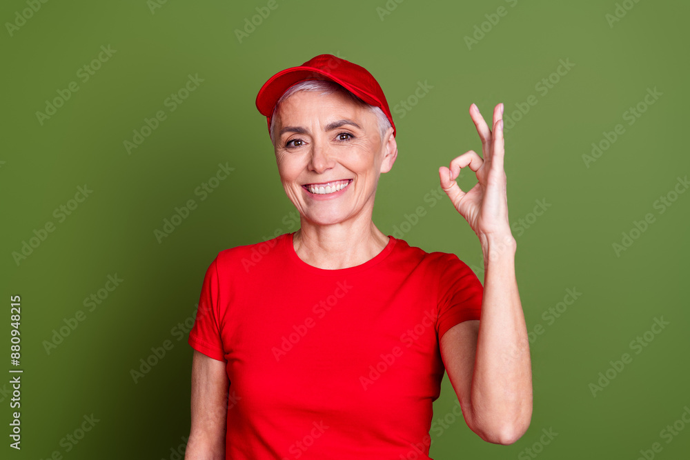 Photo of attractive mature woman professional delivery employee okey wear red uniform workwear isolated on khaki color background Photo of attractive mature woman professional delivery employee okey wear red uniform workwear isolated on khaki color background
