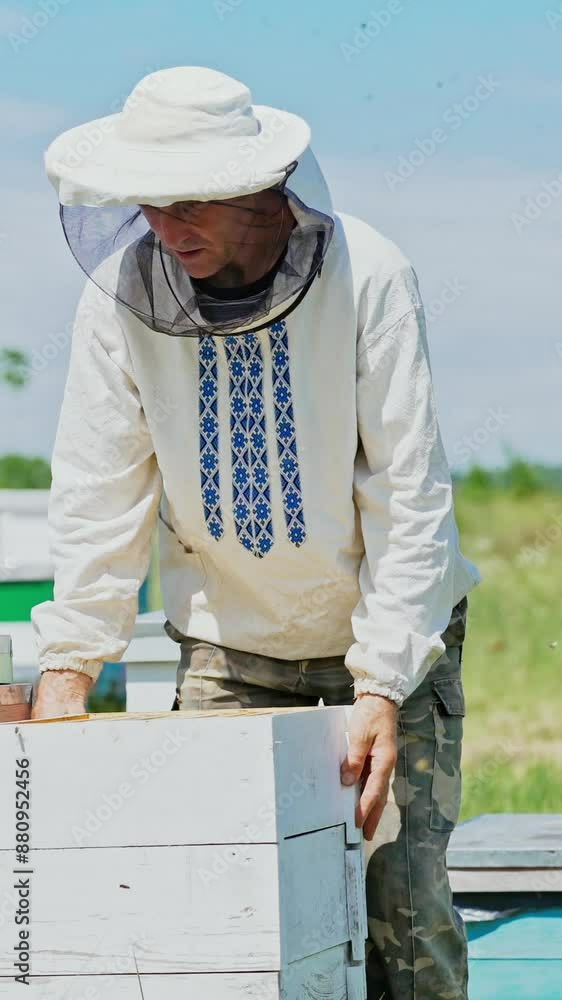 a beekeeper in protective clothing holds a frame with honeycombs for bees in the garden in the summer a beekeeper in protective clothing holds a frame with honeycombs for bees in the garden in the summer