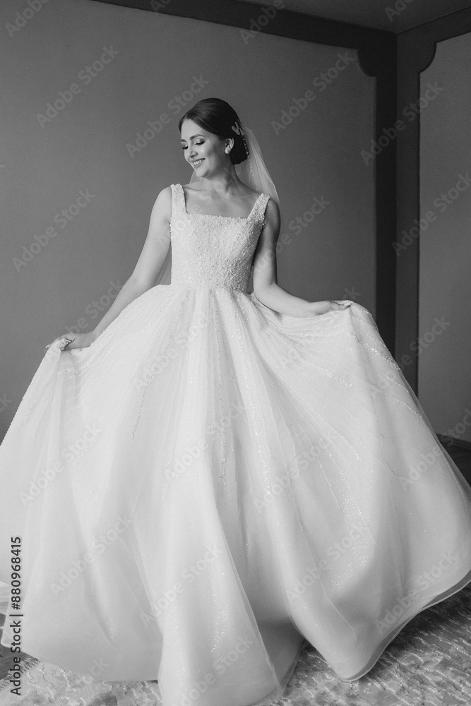 A woman in a white dress is standing in a room. She is wearing a veil and holding her dress up A woman in a white dress is standing in a room. She is wearing a veil and holding her dress up