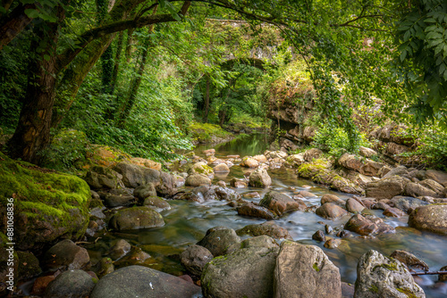 Argonza River as it passes through the medieval town of Bárcena Mayor, Cantabria, Spain, with rocks in its bed and a bridge in the background