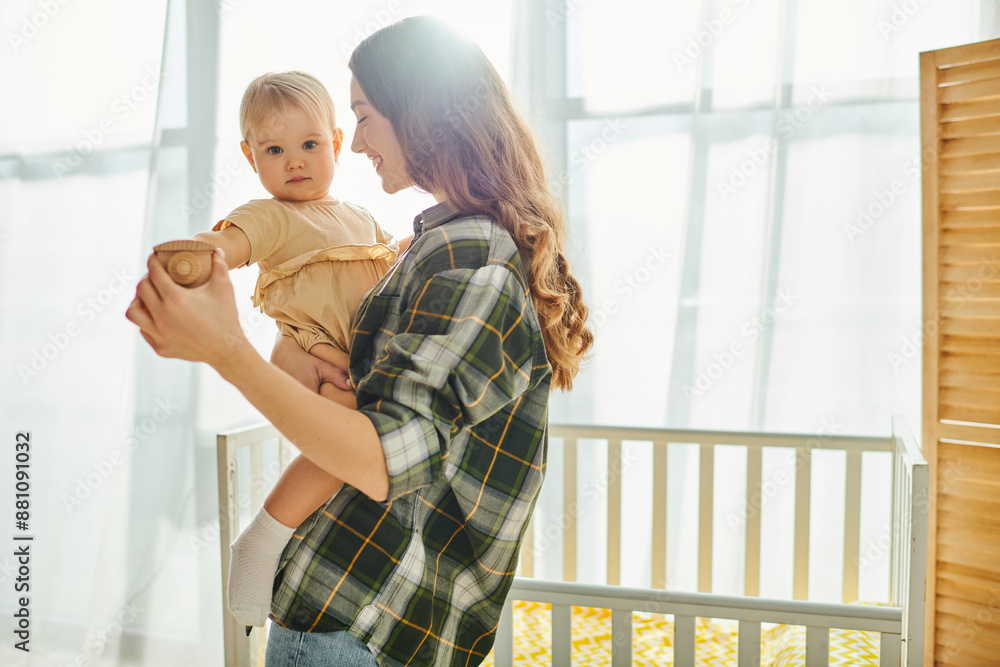 A young mother lovingly holds her toddler daughter in her arms, sharing a heartwarming moment of bonding and affection at home. A young mother lovingly holds her toddler daughter in her arms, sharing a heartwarming moment of bonding and affection at home.