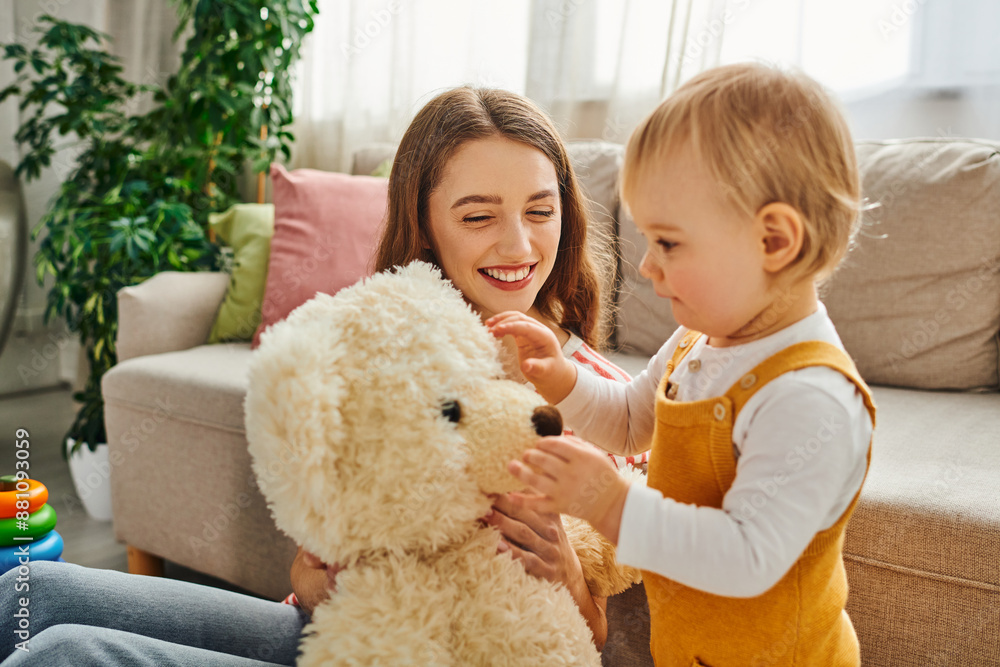 A young mother and her toddler daughter joyfully playing with a teddy bear, creating lasting memories at home. A young mother and her toddler daughter joyfully playing with a teddy bear, creating lasting memories at home.