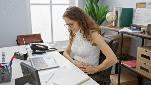 Obraz na plátně Hispanic woman feeling unwell with abdominal pain in a modern office workplace