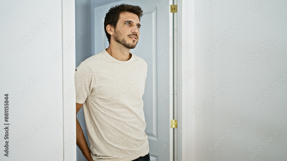 Thoughtful hispanic man with a beard standing in a bright, minimalist living room at home Thoughtful hispanic man with a beard standing in a bright, minimalist living room at home