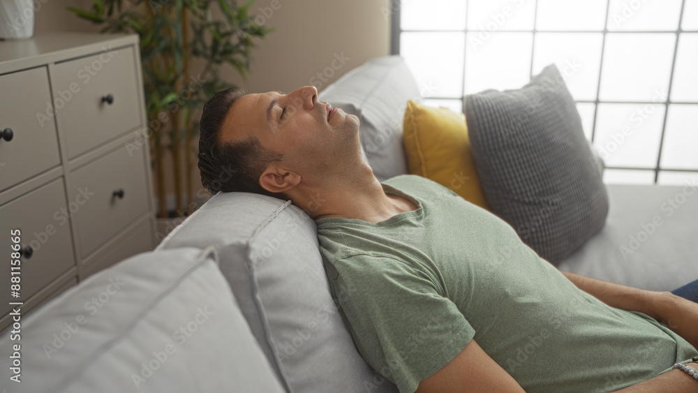 Handsome hispanic man relaxing on a couch in a living room of his home, wearing a green shirt and leaning back with closed eyes. Handsome hispanic man relaxing on a couch in a living room of his home, wearing a green shirt and leaning back with closed eyes.