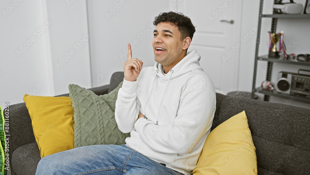 A young man in a white hoodie sitting on a sofa expresses having an idea in a modern living room setting. A young man in a white hoodie sitting on a sofa expresses having an idea in a modern living room setting.