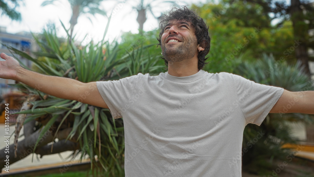 Young man enjoying a vibrant day outdoors in an urban park with arms wide open and a joyful expression Young man enjoying a vibrant day outdoors in an urban park with arms wide open and a joyful expression