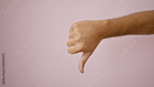 A young adult man's hand gestures a thumbs down against a pink background, expressing disapproval or rejection.