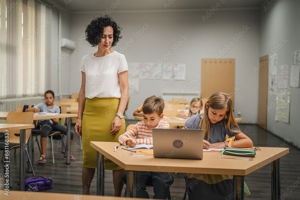 Mature teacher teach boy and girl students how to use laptop Mature teacher teach boy and girl students how to use laptop