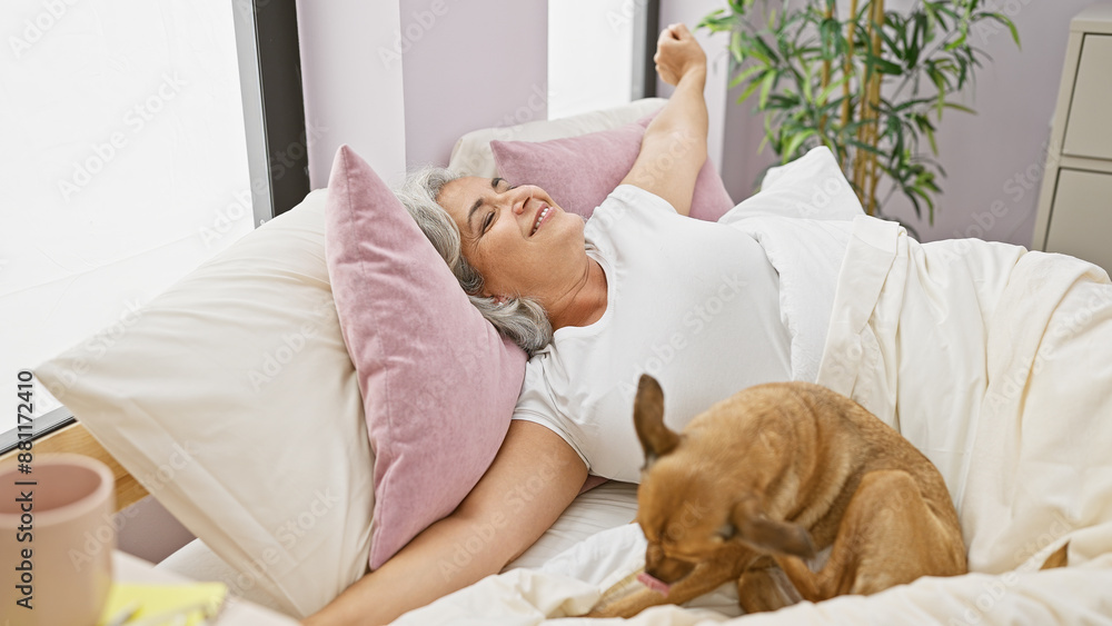 Mature woman stretching in bed with her dog in a cozy bedroom setting. Mature woman stretching in bed with her dog in a cozy bedroom setting.