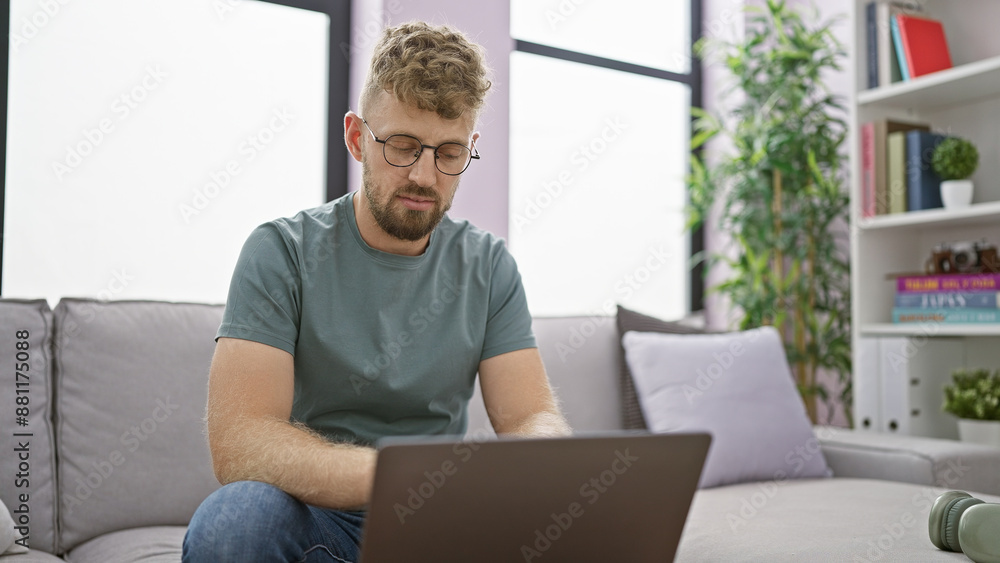 Caucasian man with beard and glasses using laptop on sofa in modern living room Caucasian man with beard and glasses using laptop on sofa in modern living room