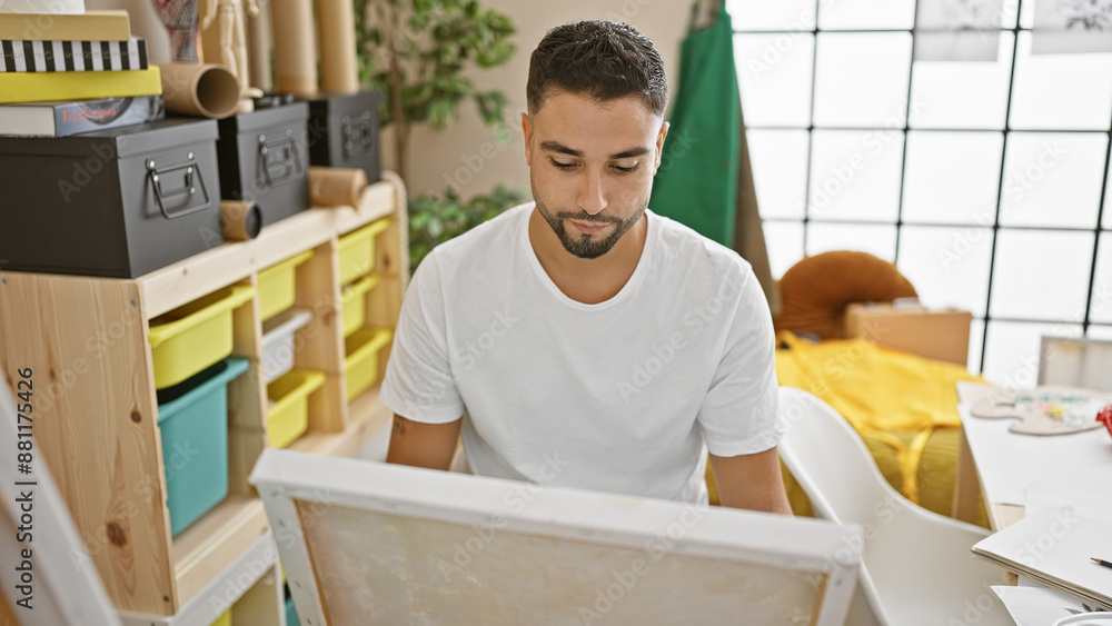 Fototapeta premium Young adult man with beard focusing on creative work in a bright art studio interior