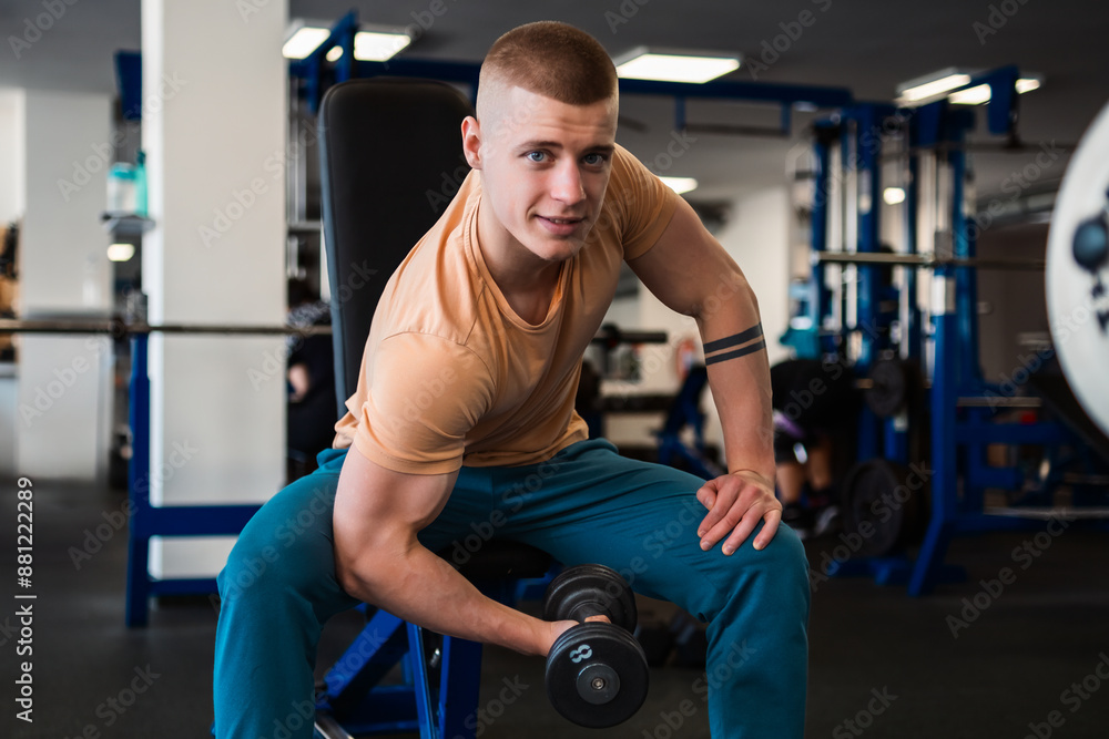 Bodybuilder performs bicep curls with a dumbbell while sitting on a bench in a gym Bodybuilder performs bicep curls with a dumbbell while sitting on a bench in a gym