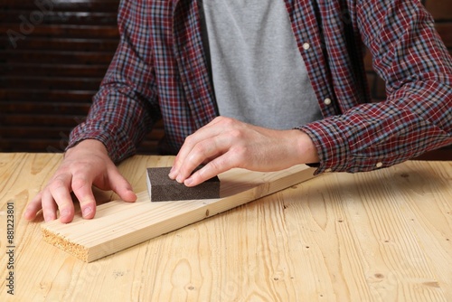 Man polishing wooden plank with sandpaper at table, closeup