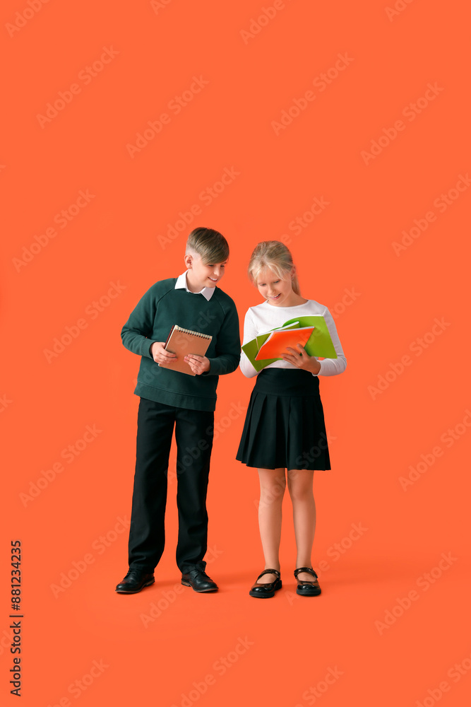 Little classmates in stylish uniform with notebooks on orange background Little classmates in stylish uniform with notebooks on orange background