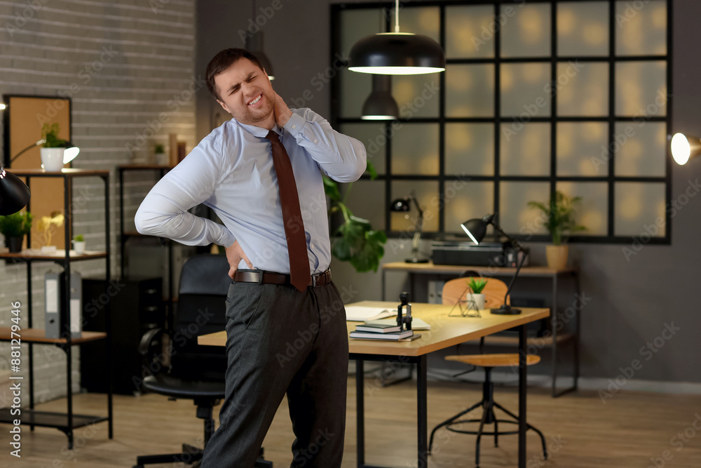 Young businessman suffering from back pain in office at night Young businessman suffering from back pain in office at night