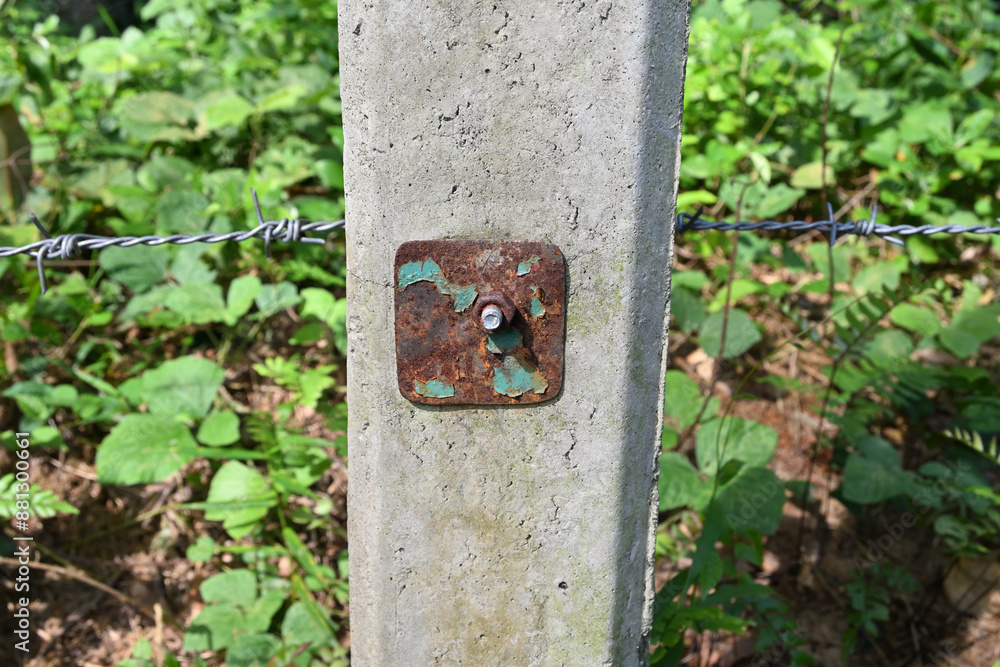 A rusty metal nut and bolt with a metal plate attached to a concrete pole on a fence A rusty metal nut and bolt with a metal plate attached to a concrete pole on a fence