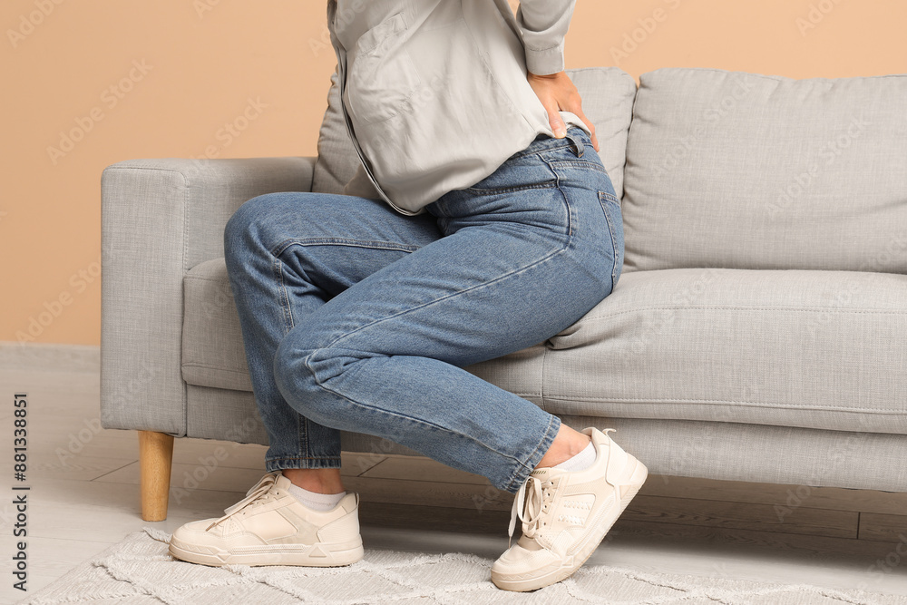 Mature woman suffering from back pain while sitting on sofa in living room Mature woman suffering from back pain while sitting on sofa in living room
