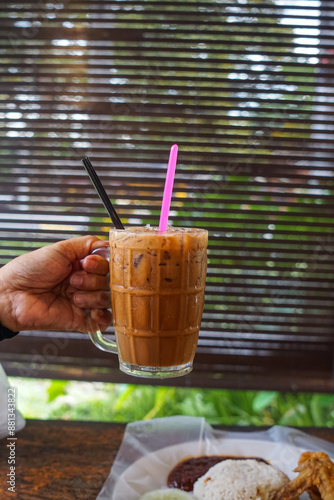 Hand holding Teh Ais or Iced Tea, sweet drink made from tea and milk, with ice cubes.