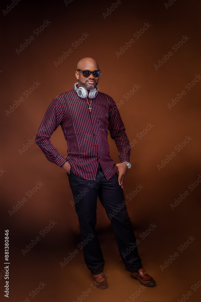 African man standing with one hand in pocket and the other hand a bit in pocket showing wrist watch wearing a corporate lined shirt and black trouser looking at camera with headset on neck African man standing with one hand in pocket and the other hand a bit in pocket showing wrist watch wearing a corporate lined shirt and black trouser looking at camera with headset on neck