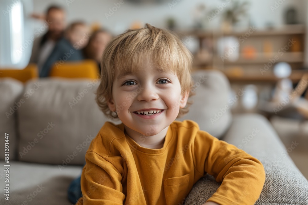 Happy and joyful three-year-old boy sitting on a couch in the living room, family smiling in the background, daylight lighting. Happy and joyful three-year-old boy sitting on a couch in the living room, family smiling in the background, daylight lighting.