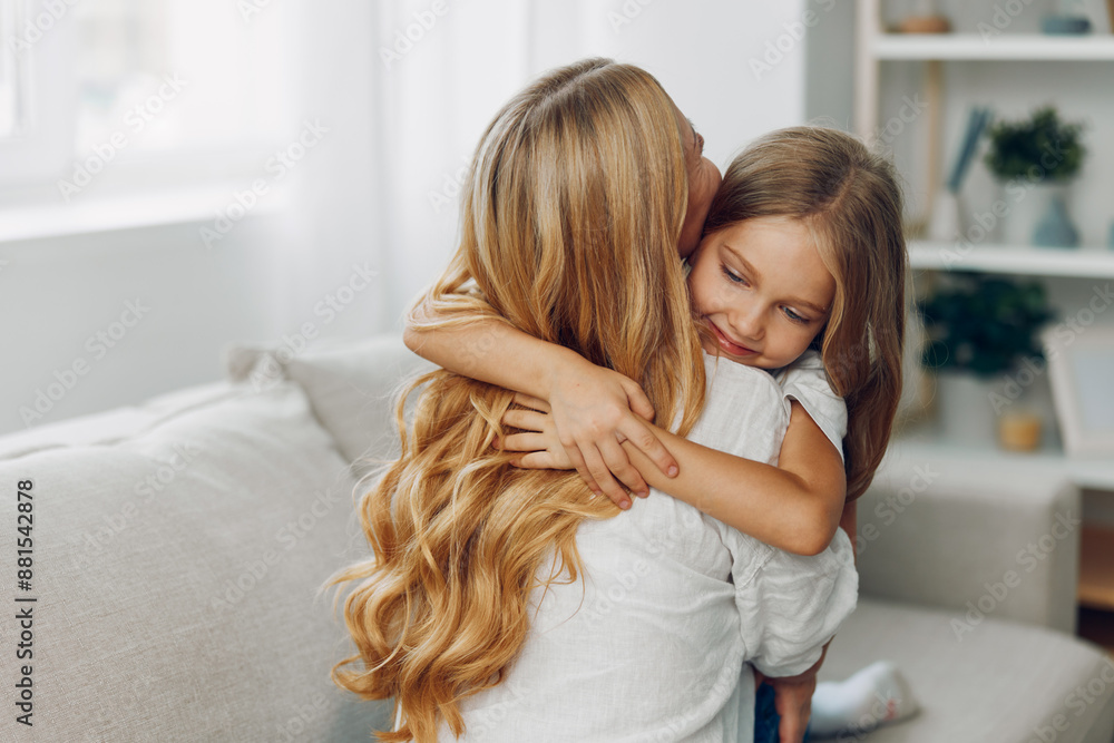 Mother and daughter sharing an emotional hug on a cozy living room couch with bookshelf in the background Mother and daughter sharing an emotional hug on a cozy living room couch with bookshelf in the background